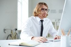 a man wearing glasses and a tie is typing on a laptop computer while sitting at a desk