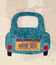 a small blue car with the word quiltin'sisa on it, sitting in front of a white wall