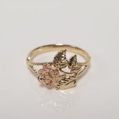 a gold ring with two leaves on the front and one pink flower on the back