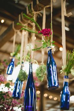 several blue vases hanging from the ceiling with flowers in them and greenery inside