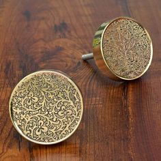 two brass colored knobs with intricate designs on them sitting on a wooden table top