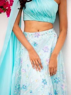 A two-piece Blue floral multi sequins lehenga with light blue drape blouse from the Shrena Hirawat collection. This beautiful cotton satin blue drape blouse is paired with a semi satin georgette blue floral multi sequins lehenga. The multi sequin floral embroidery with cancan, and butter crepe lining enhance this lehenga set. This outfit is completed with a blue dupatta attached to the drape blouse. Festive Light Blue Blouse Piece For Party, Festive Light Blue Blouse For Party, Festive Light Blue Party Blouse, Blue Silk Lehenga For Party, Summer Reception Lehenga With Unstitched Blouse, Blue Blouse Piece With Floral Embroidery For Party, Blue Silk Choli For Party, Blue Floral Embroidery Blouse Piece For Party, Blue Party Blouse With Floral Embroidery