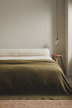 a bed with a green bedspread in a bedroom next to a wall mounted light