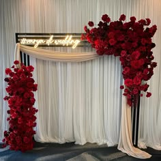 red flowers are placed on the side of a white drape draped backdrop with neon sign that says, happy new year