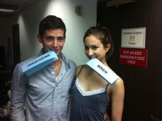 a man and woman standing next to each other holding signs in front of their mouths