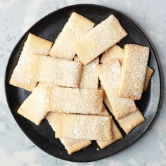 a black plate topped with cut up squares of sugary pastry on top of a table