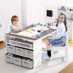 two children are sitting at a table with paint and pencils on it in the room