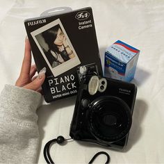 a person holding up a camera next to a box with an instax film on it