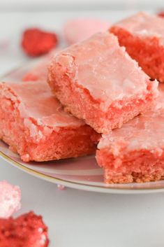 some pink frosted squares on a plate with raspberries in the back ground