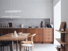 a dining room table and chairs in front of an open kitchen area with shelves on the wall