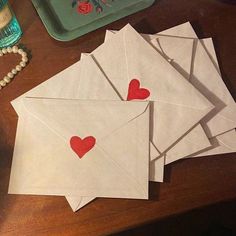 four envelopes with red hearts on them sitting on a table next to a bead necklace