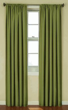 a green curtain hanging in front of a window with wood flooring and white walls