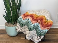 a crocheted blanket sitting on top of a wooden floor next to a potted plant