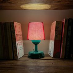 a green lamp sitting on top of a wooden table next to books and a book case