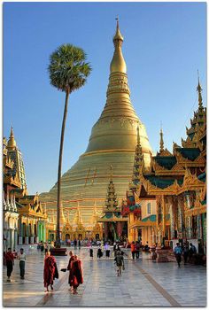 many people are walking around in front of some gold and green buildings with palm trees