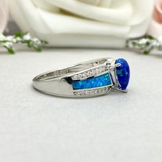 This beautiful ring is made from genuine 925 sterling silver with rhodium plating. Ring details- -The Main stone is a pear shape 8mm by 6mm Lab Created Blue Opal Stone -Side stones are Round Clear 1mm simulated diamonds and Blue Lab Created Inlay Opal -Ring is casted in solid 925 sterling silver with rhodium plating (yellow gold and rose gold plated also available, please check the drop down menu for more options) -The Total face height of the ring measures 8mms and the band width measures 2.3mm Classic Teardrop Gemstone Rings, Sterling Silver Pear-shaped Ring For Anniversary, Sterling Silver Pear Shaped Ring For Anniversary, White Gold Sterling Silver Pear-shaped Ring, Pear Shaped Sterling Silver Anniversary Rings, Pear-shaped Sterling Silver Anniversary Ring, Pear Shaped White Gold Sterling Silver Rings, Pear-shaped White Gold Sterling Silver Ring, Sterling Silver Solitaire Pear Rings