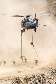 a helicopter is being lifted from the ground by ropes with other soldiers in the background