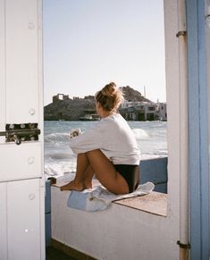 a woman sitting on top of a wall next to the ocean