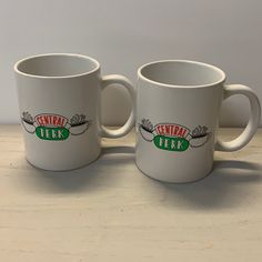 two white coffee mugs sitting on top of a wooden table next to each other