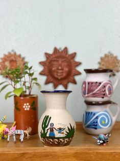 three vases are sitting on a shelf next to small plants and figurines