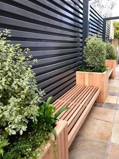 a wooden bench sitting in front of a black wall next to potted planters