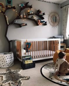 a baby sitting in a crib next to a tree with lights on the branches