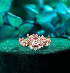 a pink diamond ring sitting on top of a green velvet covered table next to leaves