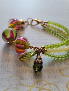 This bright beautiful bracelet is perfect for a casual dressy outfit. It has 3 large Pink and Green beads with multi strands of green beads. The clasp and accent beads are gold. This would look great with a boho skirt! Large Beaded Bracelets, Bohemian Bracelets With Dangling Beads, Bohemian Green Bracelets, Green Czech Glass Spiritual Beads, Spiritual Green Czech Glass Beads, Bohemian Multi-strand Bracelets With Large Beads, Bohemian Multi-strand Green Beads, Bohemian Green Multi-strand Beads, Bohemian Green Bracelets With Spacer Beads