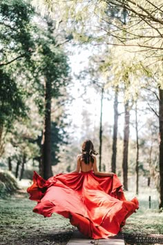 a woman in a red dress is walking through the woods with her back to the camera