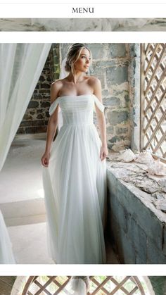 a woman in a white dress standing next to a window