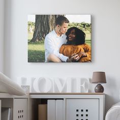 a man and woman embracing each other in front of a white wall with the word home on it