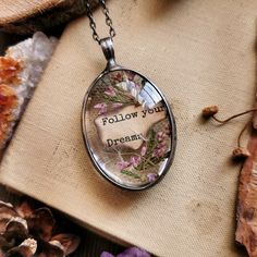 a glass pendant with the words follow your dream on it sitting next to dried flowers