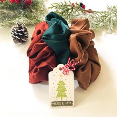 three different colored hair scrunffs on a white table next to pine cones and christmas decorations