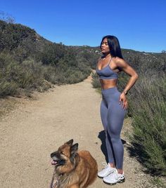 a woman standing next to a dog on a dirt road