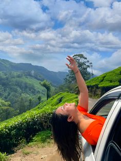 a woman leaning out the window of a car on a road with mountains in the background