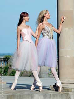 two young ballerinas dressed in pink and lavender tutu skirts are standing next to each other