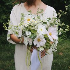 a woman holding a bouquet of white and green flowers in her hands with grass behind her