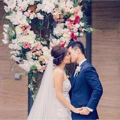 a bride and groom standing in front of a floral arch with flowers on it's side