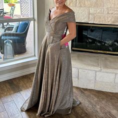 a woman standing in front of a fire place wearing a gold dress and smiling at the camera