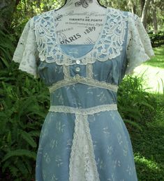 "Today I have a Vintage, Gunne Sax dress of a muted, Fall blue (medium weight cotton) with cream-colored posies and heavy lace adornments. The silhouette is an Aline and the waist is in the high, empire style. The bodice is adorned with heavy, floral lace that is tightly woven to produce a sheen and 3 buttons are in place vertically for interest below a privacy panel. Heavy weight, floral lace comprises the flutter sleeves and is also present on the apron. As stated above, the waist is high and Blue Cotton Dress With Lace Patchwork, Blue Yoke Dress For Spring, Light Blue Bohemian Dress With Lace Trim, Flowy Cotton Vintage Dress, Flowy Vintage Cotton Dress, Fitted Summer Dress With Yoke Detail, Summer Fitted Dress With Yoke Detail, Summer Fitted Yoke Dress, Blue Fitted Cottagecore Dress