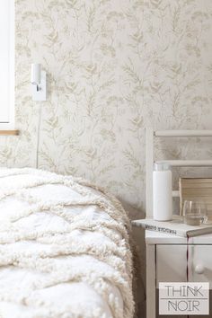 a white bed sitting under a window next to a wall mounted phone charger and lamp