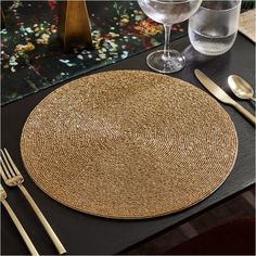 a place setting with silverware and wine glasses on a black table cloth, along with gold flatware