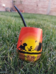 a painted cup sitting in the grass on top of green grass with an orange and yellow background