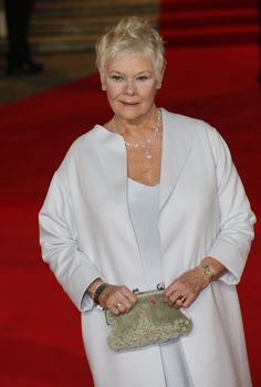 an older woman wearing a white coat and holding a green purse on a red carpet