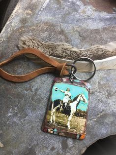 a keychain with an image of a man on a horse next to a feather