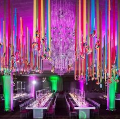 a room filled with lots of tables covered in white tablecloths and colorful chandeliers