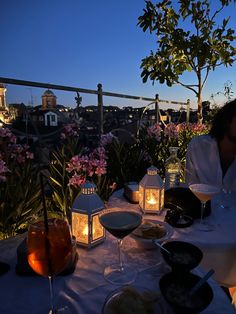 a man and woman sitting at a table with wine glasses on it, overlooking the city