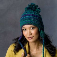 a woman wearing a green and blue knitted hat with pom - poms