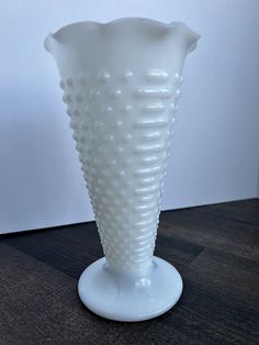 a white glass vase sitting on top of a wooden table in front of a wall