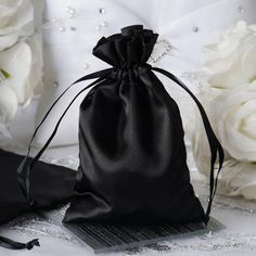 a black satin bag sitting on top of a table next to white flowers and pearls